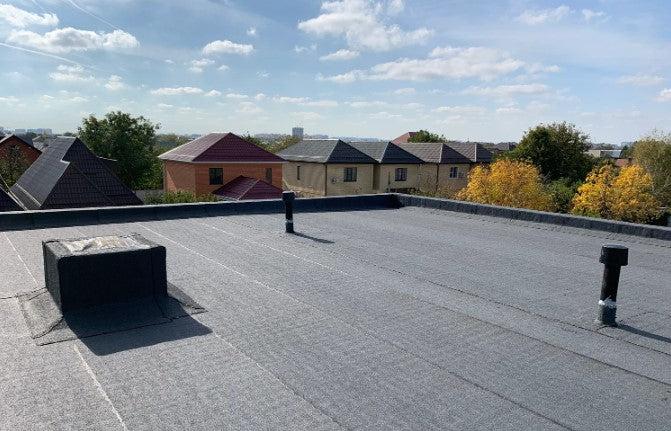 Плоски покриви с хидроизолация, гледка към подобни сгради на фона на синьо небе и облаци.